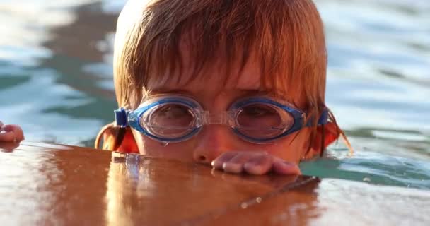 スイミングプールで子供 プールサイドに保持ゴーグルを身に着けている若い男の子の顔のクローズアップ — ストック動画