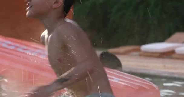 スイミングプールの水の中の若い男の子の子供に水を飛ばす — ストック動画
