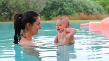 Mom holding newborn baby inside swimming pool water