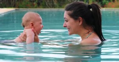 Mother holding baby son inside swimming pool water interaction
