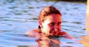 Havuzda yüzen bir kadın kameraya bakıyor.