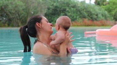 Mom holding newborn baby inside swimming pool water