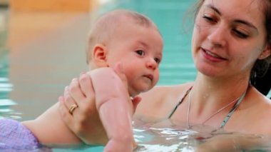 Mom holding baby boy inside swimming pool water