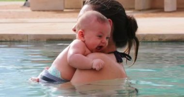 Mother holding baby at the swimming pool water, mom kissing her infant son