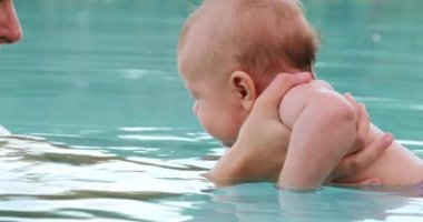 Mother holding baby son inside swimming pool water interaction