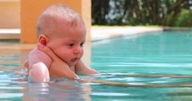 Mother and baby infant at the pool together interaction. Mom kissing and hugging baby son, showing love and affection