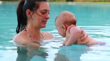 Mom holding baby boy inside swimming pool water