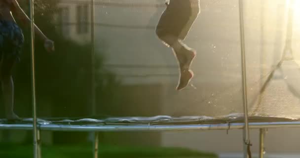 屋外でトランポリンの中に飛び込む子供たちとレンズフレアの日差しが輝く — ストック動画