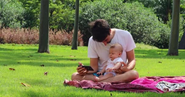 Padre Bebé Juntos Sentados Parque Mirando Dispositivo Teléfono Inteligente Aire — Vídeo de stock