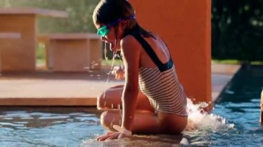 Çocuk havuzda oynuyor. Su sıçrıyor. Yavaş çekimde küçük bir kız oynuyor.