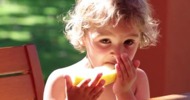 Portrait of cute little blonde boy eating melon fruit outdoors