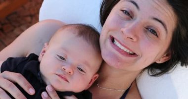 Mother holding baby infant son looking to camera smiling