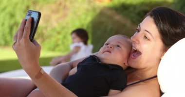Mother taking selfie with her baby outdoors smiling posing for photo