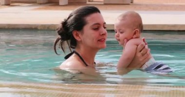 Candid mother holding baby infant at the swimming pool showing love and affection