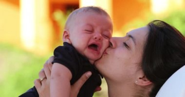 Mother kissing crying baby infant son showing love and affection outdoors