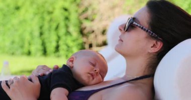 Candid mother and baby together taking nap mom wakes up and waves to camera removing sunglasses