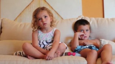 Çocuklar kanepede oturmuş televizyon izliyorlar.