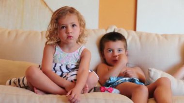 Çocuklar kanepede oturmuş televizyon seyrediyor. Küçük kız ve oğlan ekranla hipnotize oluyor.