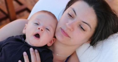 Baby on top of mother yawning looking to camera