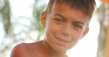 Child looking to camera smiling portrait of young boy outside with lens-flare sunlight