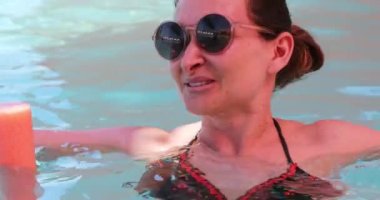 Havuzda yuvarlak güneş gözlüğü takan bir kadın.