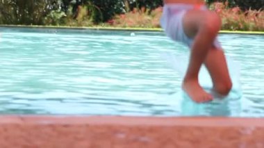 Çocuk havuz suyuna yavaş atlıyor.