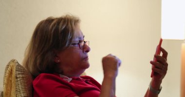 Normal yaşlı kadın cep telefonunu kontrol ediyor öksürüyor ve ekrana dokunuyor.