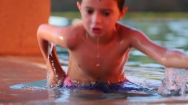 Küçük çocuk havuzdan yavaş çekimde çıkıyor çocuk ayakları ayakta ve su sıçrıyor