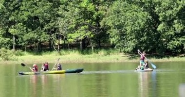Çocuklar göl kenarında kanonun içinde kano yapıyor.