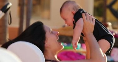 Candid mother holding baby infant outside by the poolside having fun
