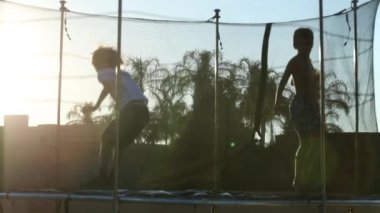 Çocuklar gün batımında dışarıda trambolinde zıplıyorlar.