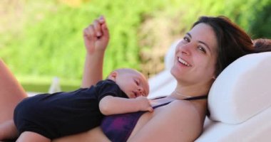 Woman spontaneous real life laugh and smile outside by the pool with baby happy mother