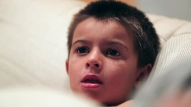 Young boy hypnotized by TV screen seated at home sofa at night