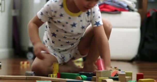 Infant boy playing with building wooden toys in room destroying structure