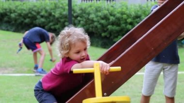 Children playing at playground toddler holding into slider