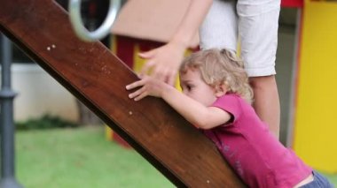 Brother helping baby toddler sibling at playground climbing slider