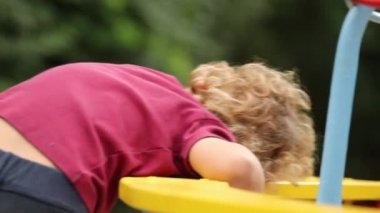 Cute toddler boy playing at park with spinning carousel