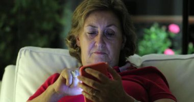 Older senior woman holding smartphone device touching screen at night