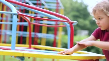 Child boy making carousel spin at playground outdoors