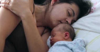 Newborn baby and mother sleeping together in bed, candid real life family moment