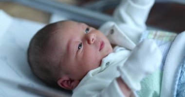 Newborn baby at hospital nursery after birth, first day of infant life inside crib