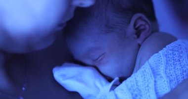 Mother holding newborn baby at hospital next to violet phototherapy lamp, real life affection and love