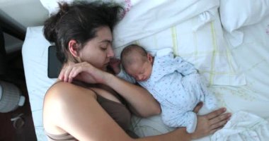 Candid newborn baby and mother together in bed waking up in the morning, vertical from above