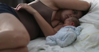 Candid tired young mother next to newborn baby waking up worried, going back to sleep