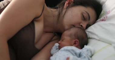 Candid family moment of mother and newborn asleep in bed
