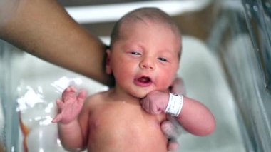 Newborn baby taking bath for the first time. Infant boy in warm bath