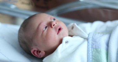 Newborn baby at hospital nursery after birth, first day of infant life inside crib
