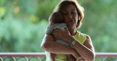 Grand-mother holding newborn baby grand-son in outside balcony