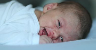 Cute happy newborn baby smiling feedling joy, infant first week of life in bed