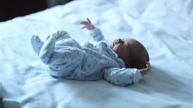 Cute tiny newborn baby stretching body in bed, first days of life